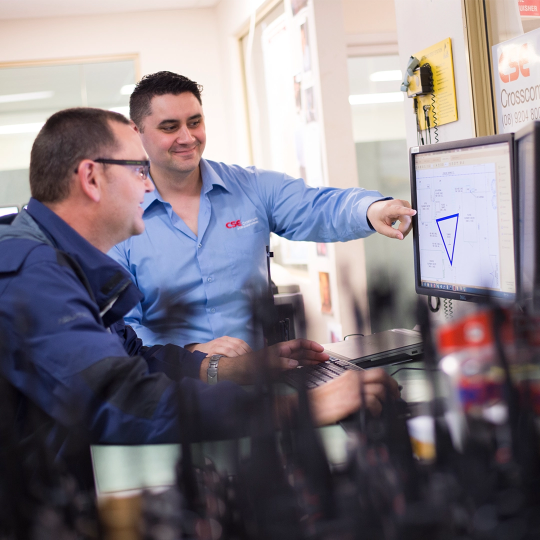 Two CSE Crosscom technicians in a well-lit office point at a schematic on a computer monitor.